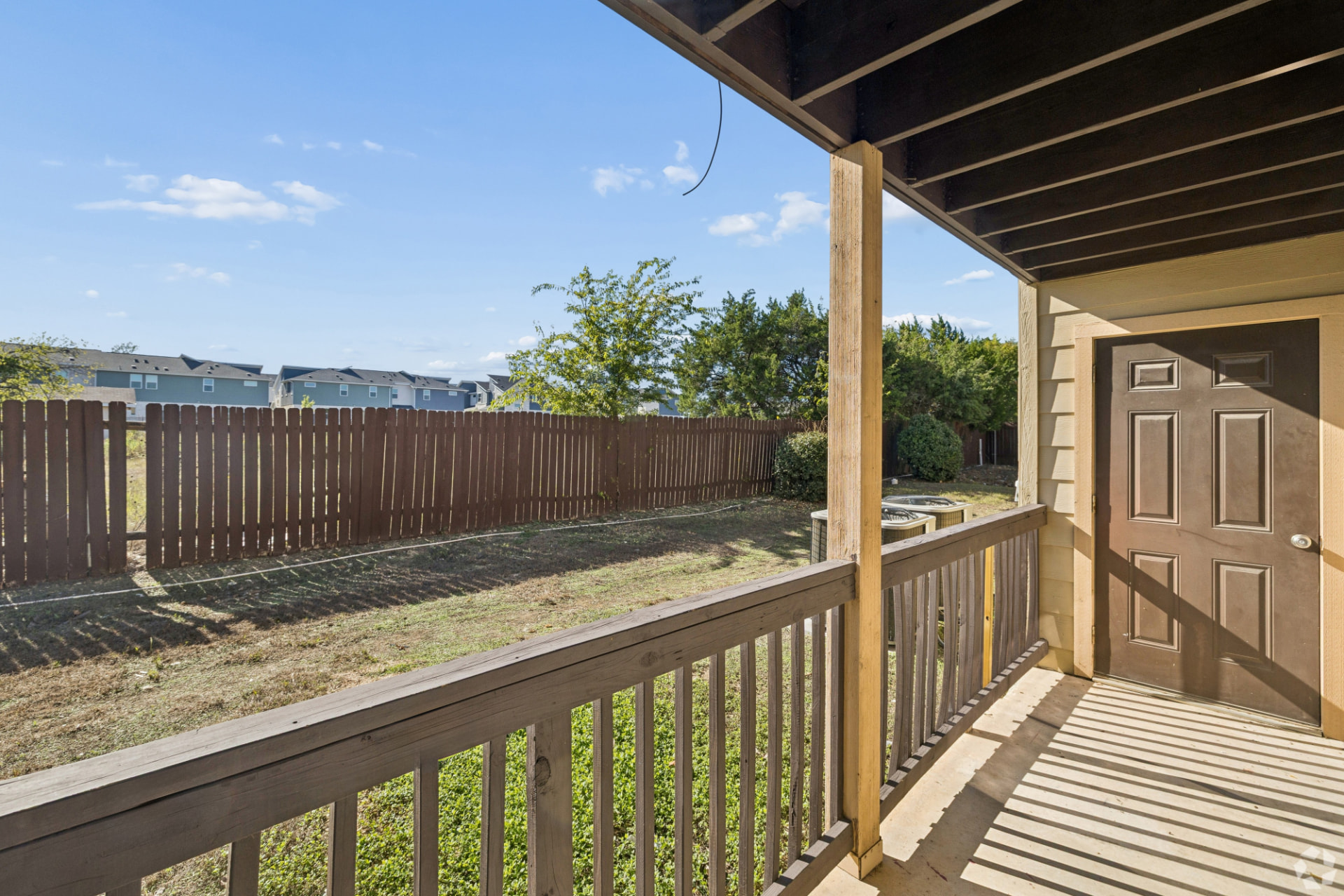 Covered ground-floor porch with wood spindle railing and concrete floor at a renovated home