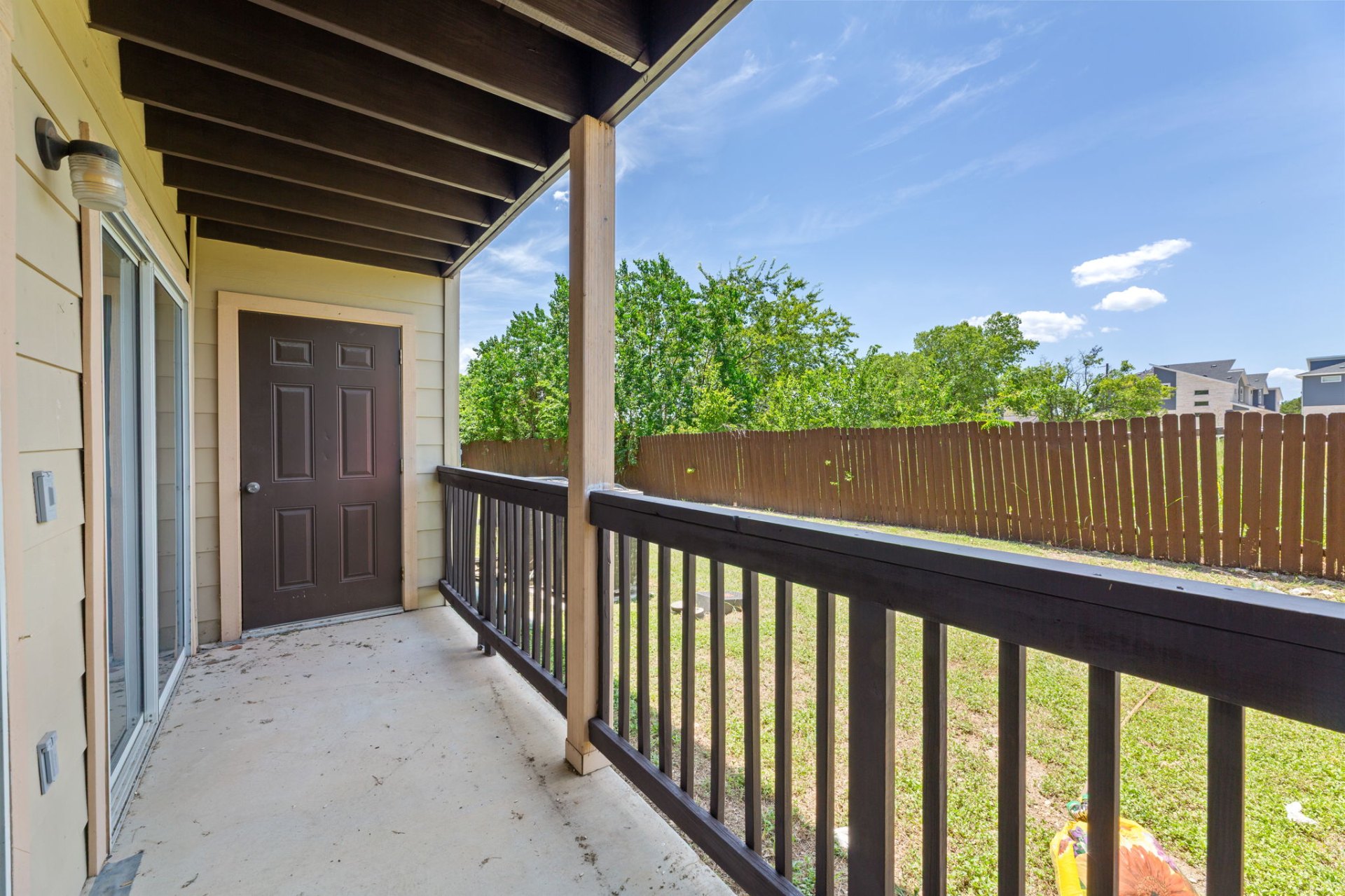 Private covered back balcony with wood railing, overlooking the fenced yard