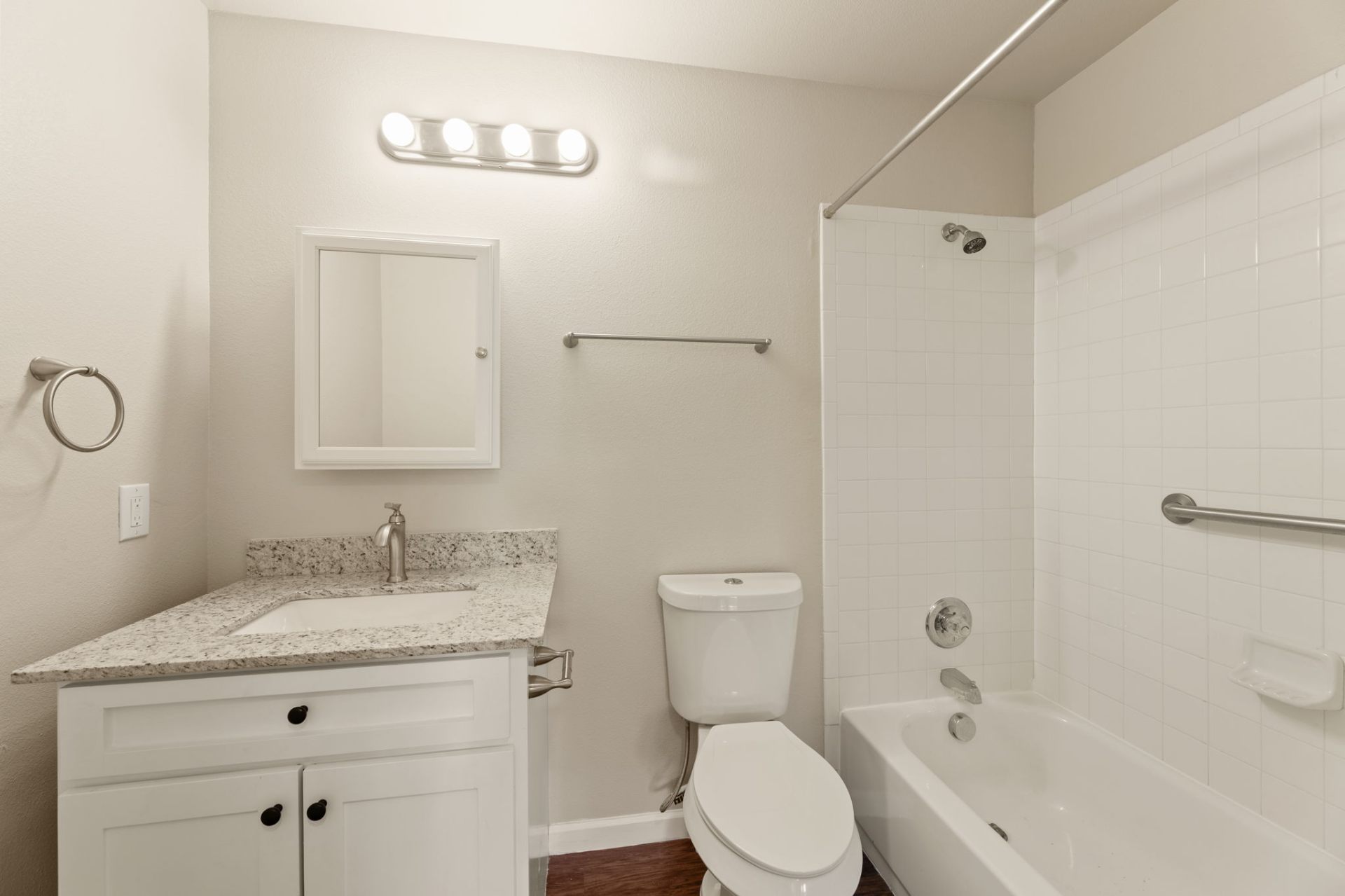 Full bathroom with granite vanity, framed mirror, and tiled tub surround