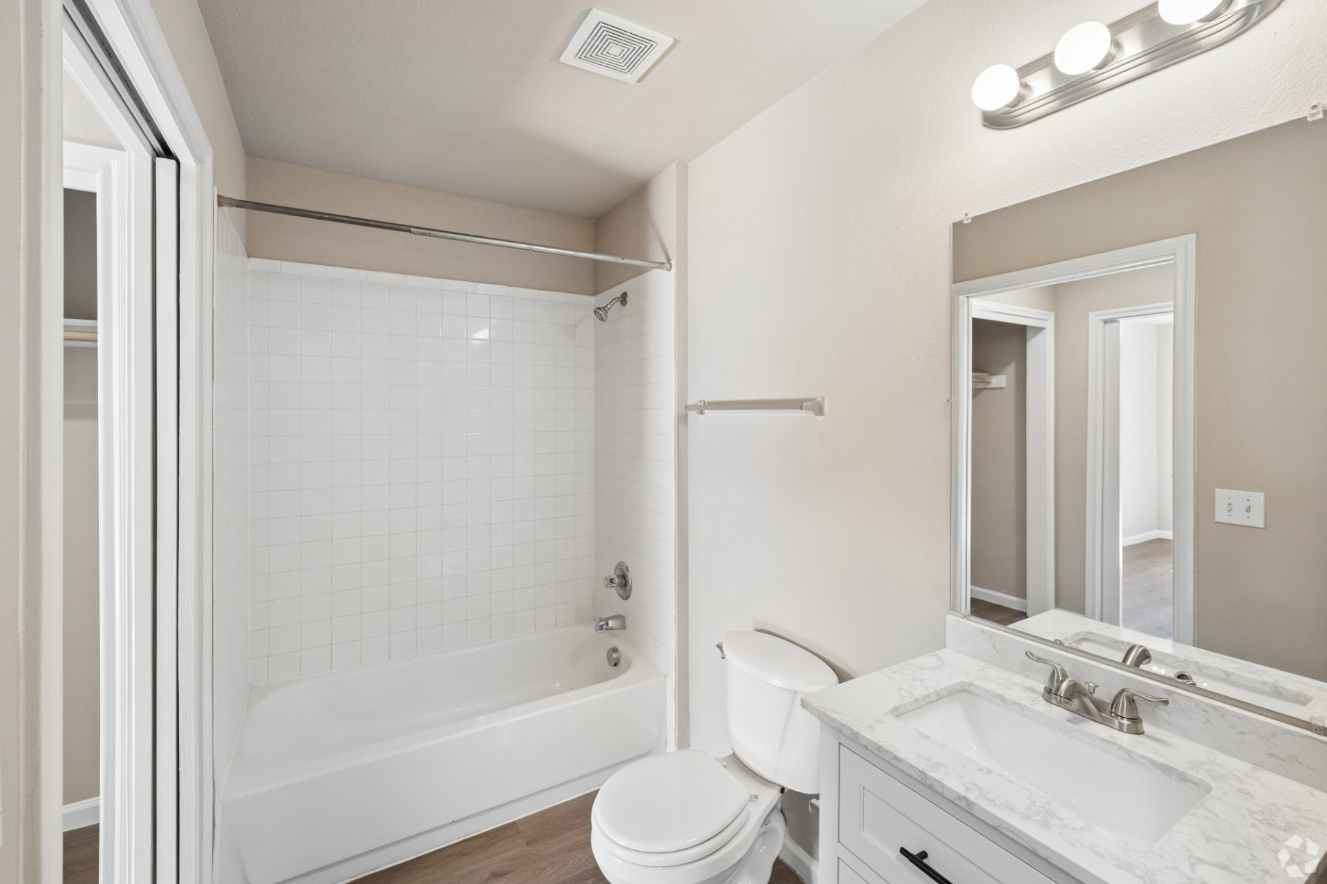 Renovated bathroom with white vanity, marble-look counter, white tile tub surround, and wood-look flooring