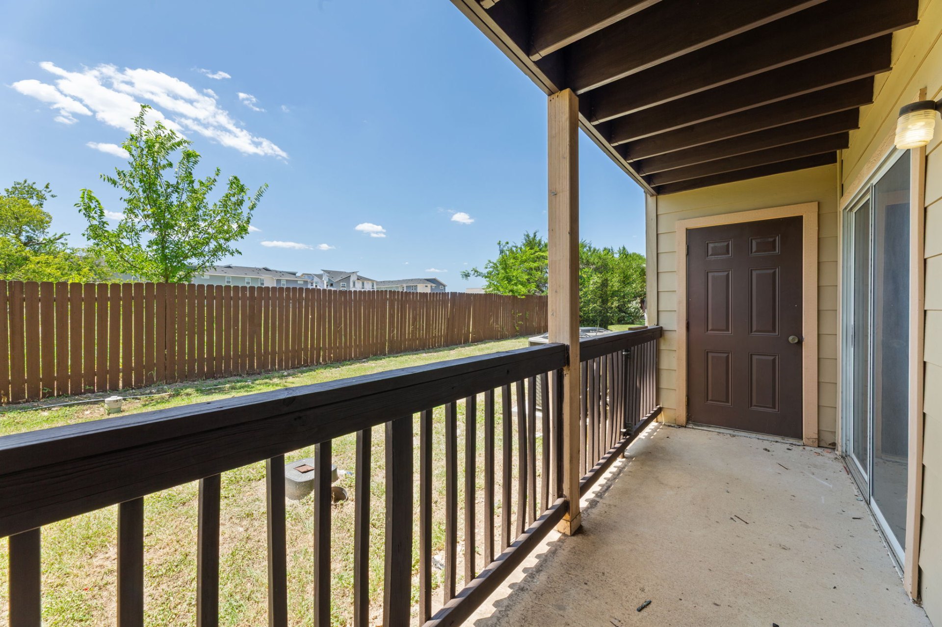 Private covered patio with wood railing overlooking the fenced yard (classic-finish home)